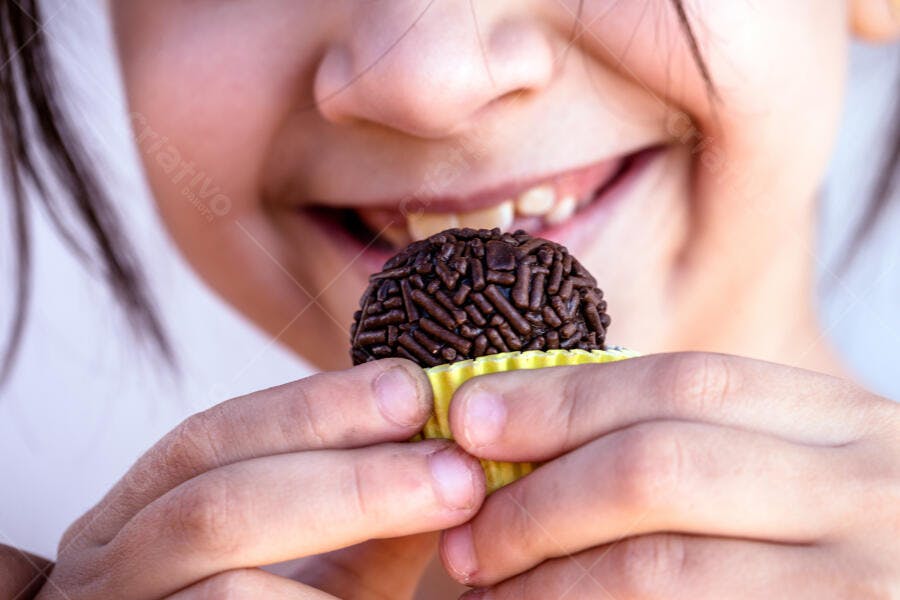 Menina feliz com brigadeiro de chocolate em forminha amarela