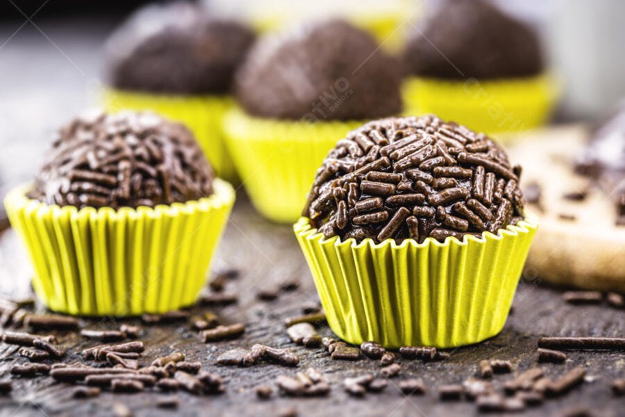 Brigadeiro de chocolate com granulado em forminha amarela sobre mesa de madeira escura