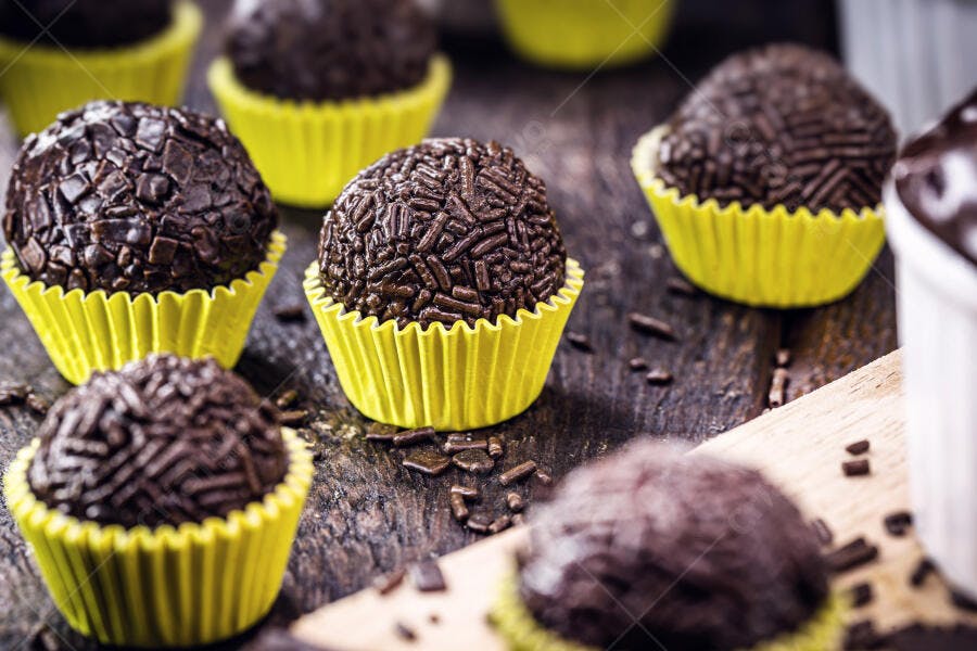 Brigadeiros doces brasileiros em forminhas amarelas sobre mesa de madeira rústica