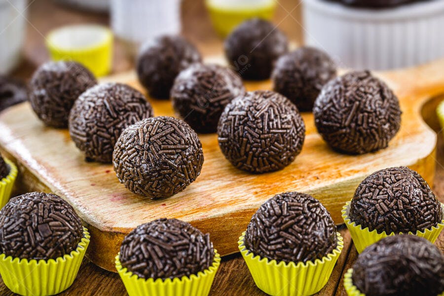 Doces brigadeiros brasileiros de festa em forminhas amarelas sobre tábua rústica