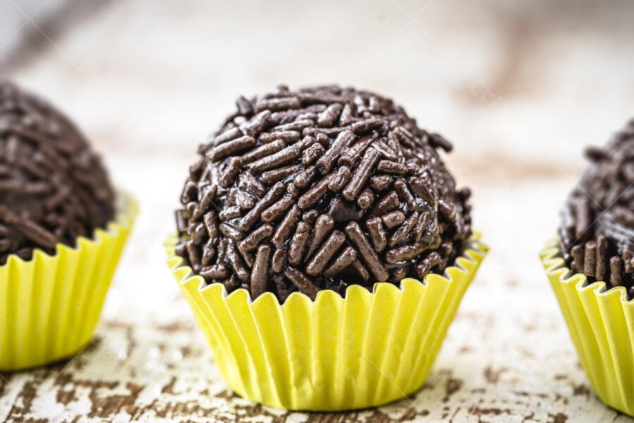 Brigadeiro de chocolate com granulado em forminha amarela sobre madeira rústica