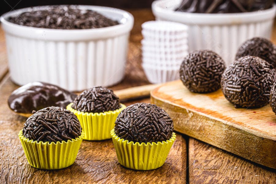 Brigadeiros de chocolate com granulado em forminhas amarelas sobre mesa de madeira