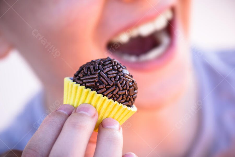 Pessoa sorrindo saboreando brigadeiro de chocolate escuro em forminha amarela
