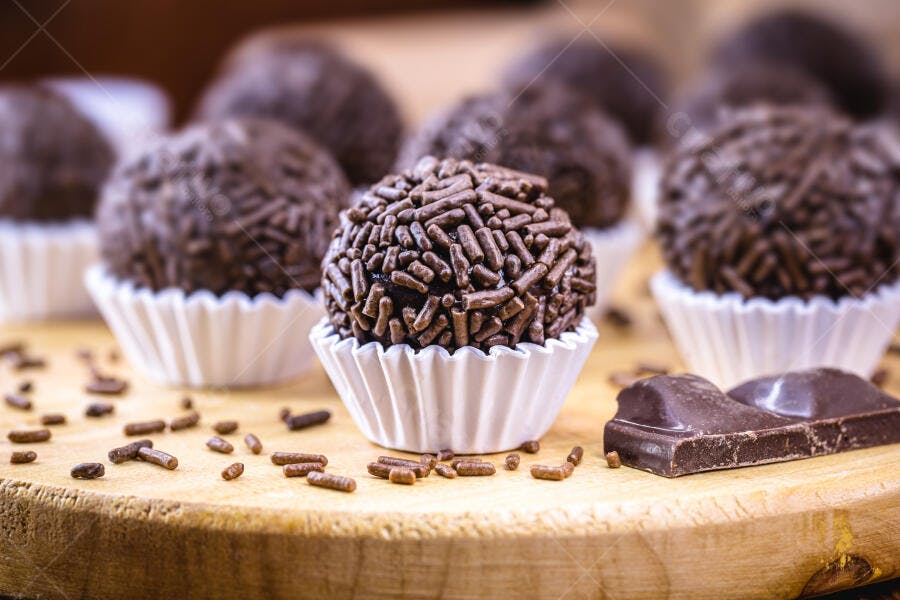 Brigadeiros de chocolate com granulado em forminhas brancas na tábua de madeira