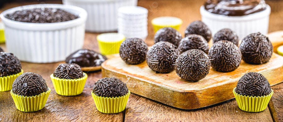 Brigadeiros de chocolate com granulado em forminhas amarelas sobre mesa de madeira
