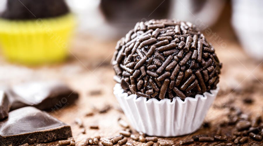 Brigadeiro de chocolate com granulado em forminha branca sobre madeira