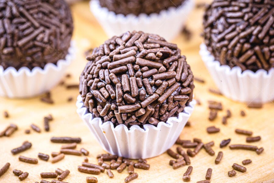 Brigadeiro de chocolate com granulado em forminha branca sobre mesa de madeira claro