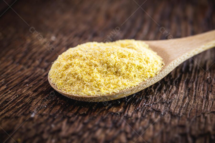 Farinha de mandioca amarela na colher de pau em mesa de madeira rústica