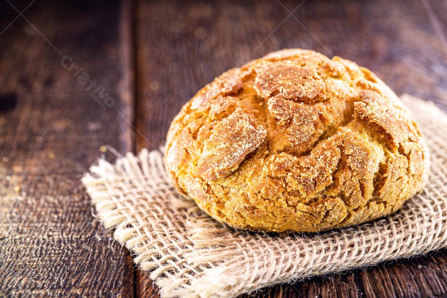 Pão de milho dourado rústico sobre tecido de juta em mesa de madeira escura