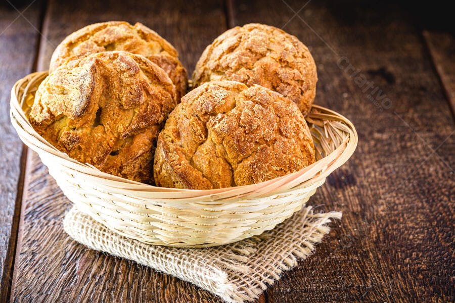Pães de fubá dourados em cesta de vime sobre mesa de madeira rústica