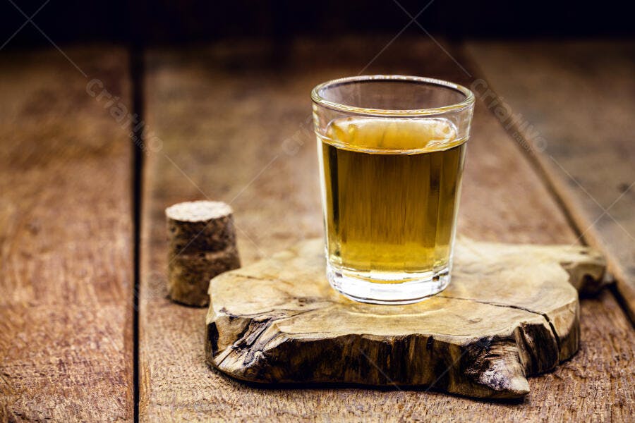 Copo de cachaça amarela sobre madeira rústica e rolha de cortiça
