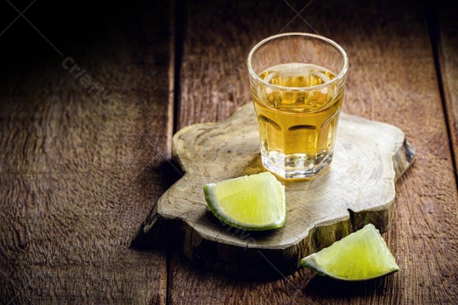 Copo de cachaça ou tequila com limão em tábua de madeira rústica