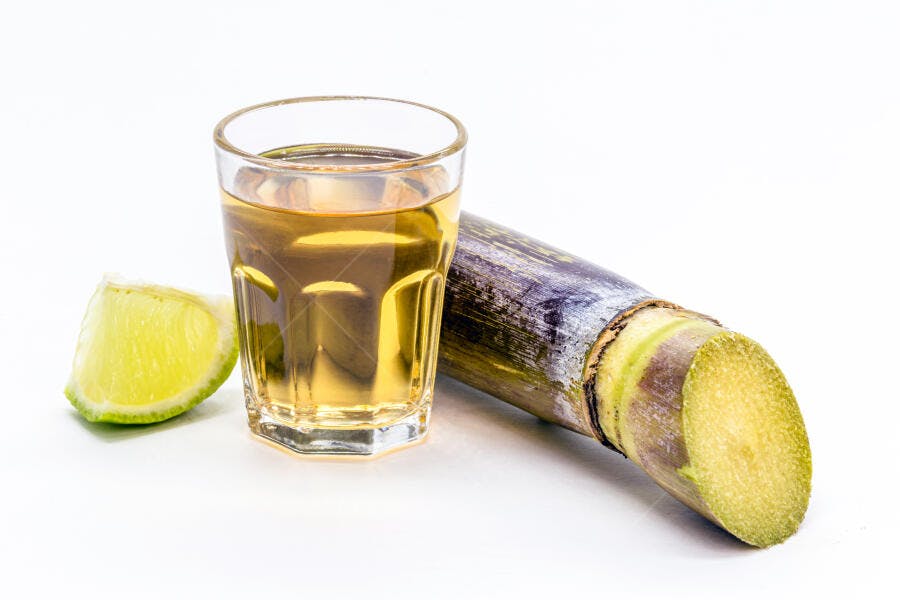 Cachaça dourada em copo de dose com limão e cana-de-açúcar em fundo branco