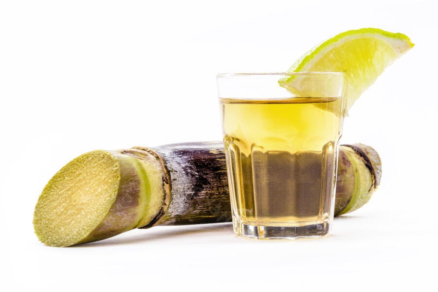 Cachaça em copo com limão e cana-de-açúcar roxa fresca fundo branco