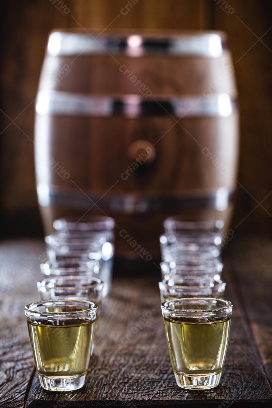 Shots de destilado dourado em mesa de madeira com barril no fundo ambiente rústico
