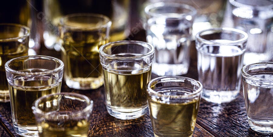Copos de shot com bebidas claras e douradas em superfície de madeira rústica
