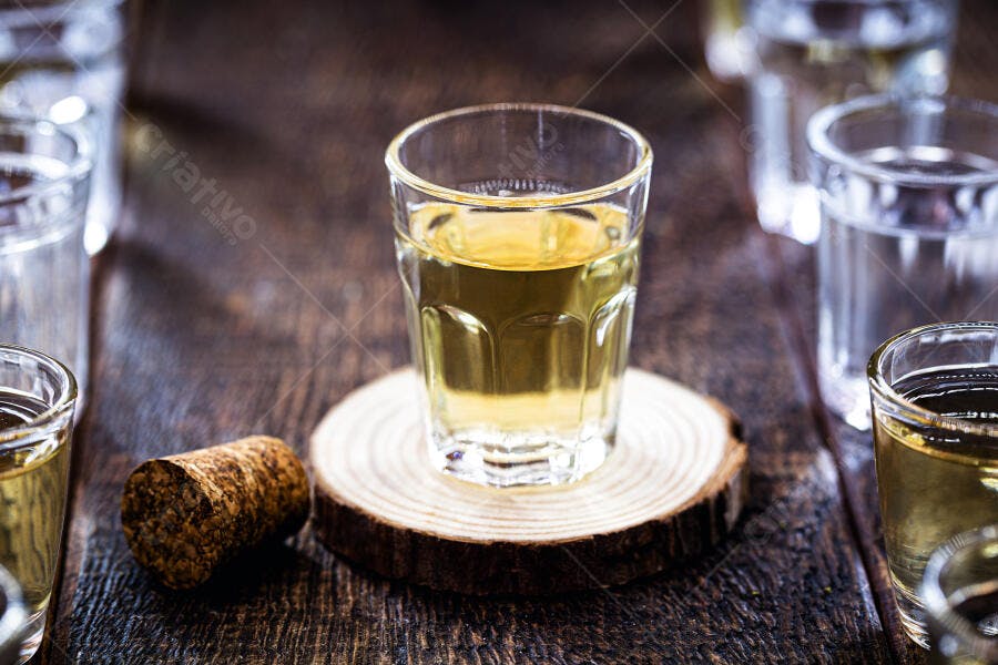 Cachaça dourada em copo rústico sobre mesa de madeira escura e rolha