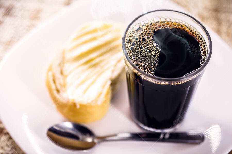 Café preto quente com pão na chapa e colher em prato branco