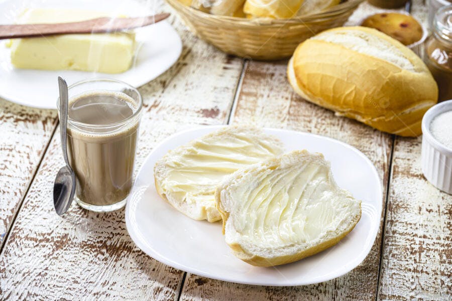 Pão francês com manteiga fumegante e café com leite em mesa rústica de café da manhã