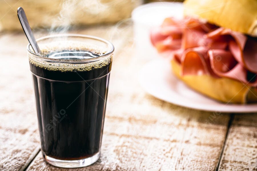 Café quente em copo com sanduíche de mortadela na mesa rústica