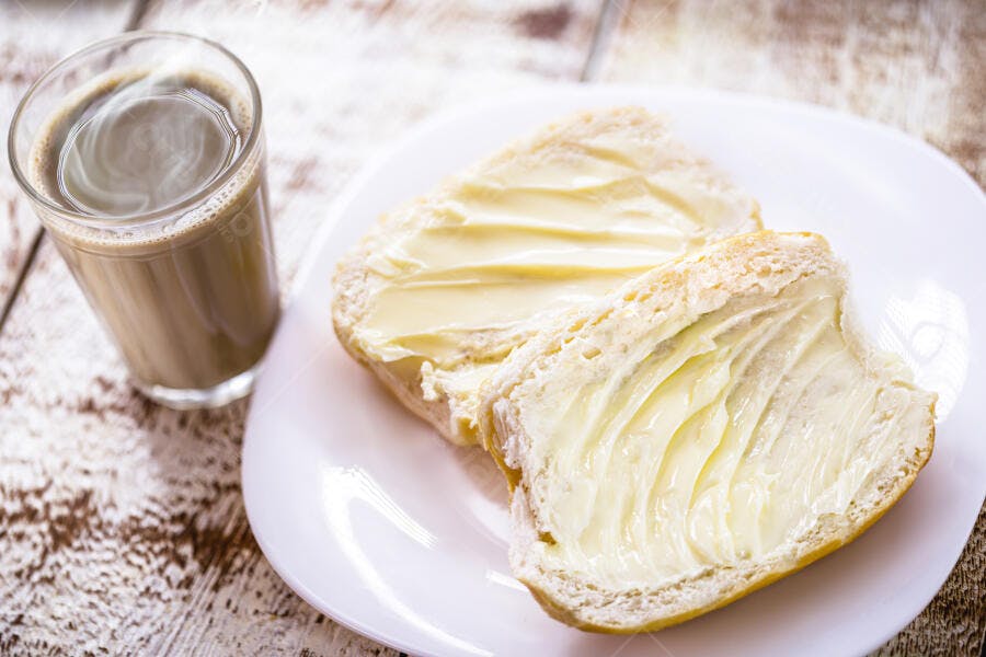 Pão francês com manteiga e café com leite em mesa rústica para café da manhã