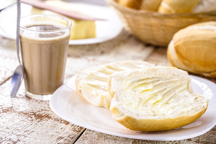 Pão francês com manteiga e café com leite em mesa rústica de café da manhã