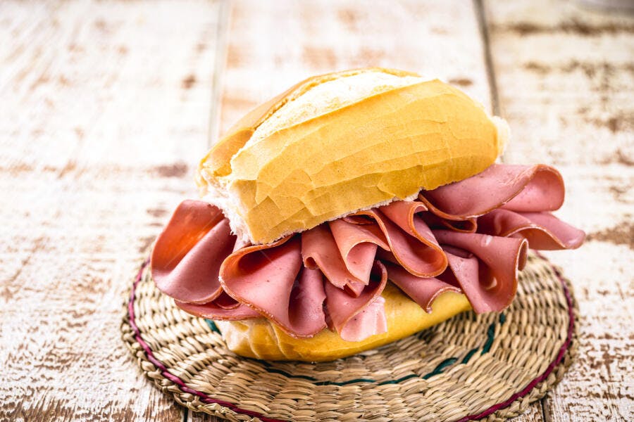 Sanduíche de mortadela com pão francês em mesa rústica de madeira clara