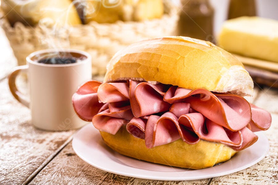 Sanduíche de mortadela com pão francês e café fumegante em mesa de madeira