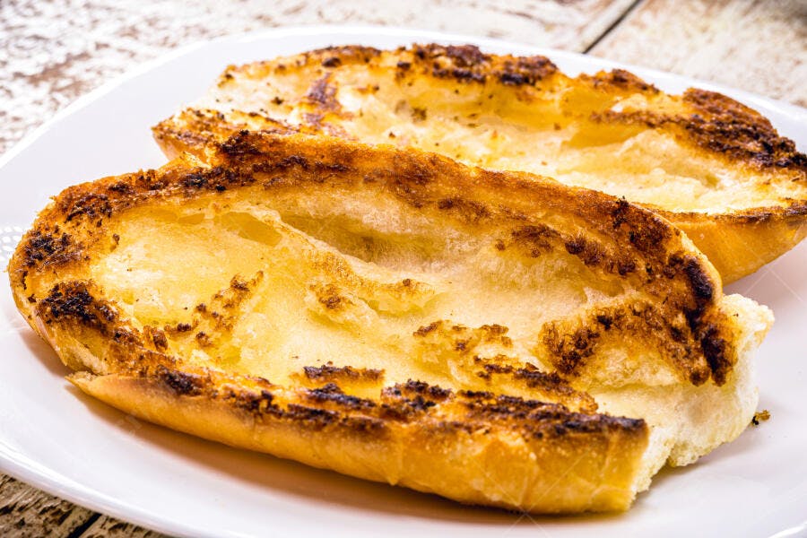 Pão torrado crocante na chapa em prato branco sobre madeira