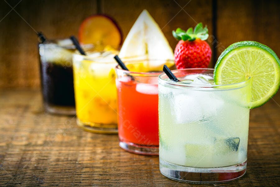 Coquetéis tropicais coloridos com frutas frescas e gelo em mesa de madeira