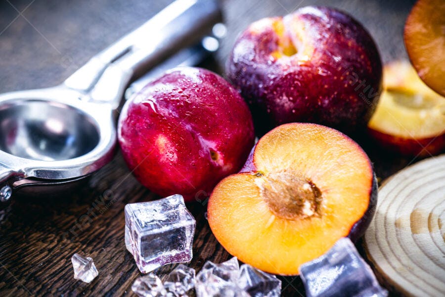 Ameixas frescas cortadas com gelo e espremedor de frutas em fundo de madeira rústica