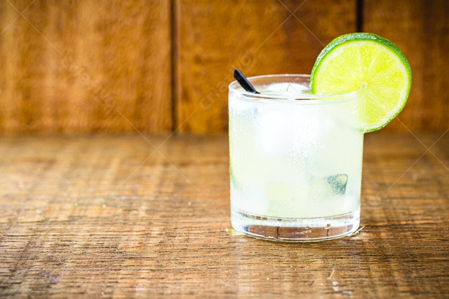 Copo de caipirinha gelada com fatia de limão em mesa de madeira rústica
