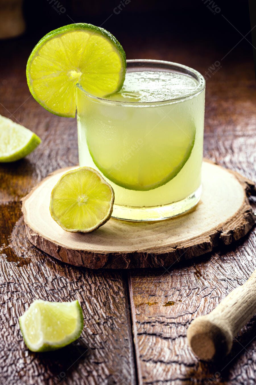 Caipirinha gelada com rodelas de limão e pilão sobre mesa de madeira rústica