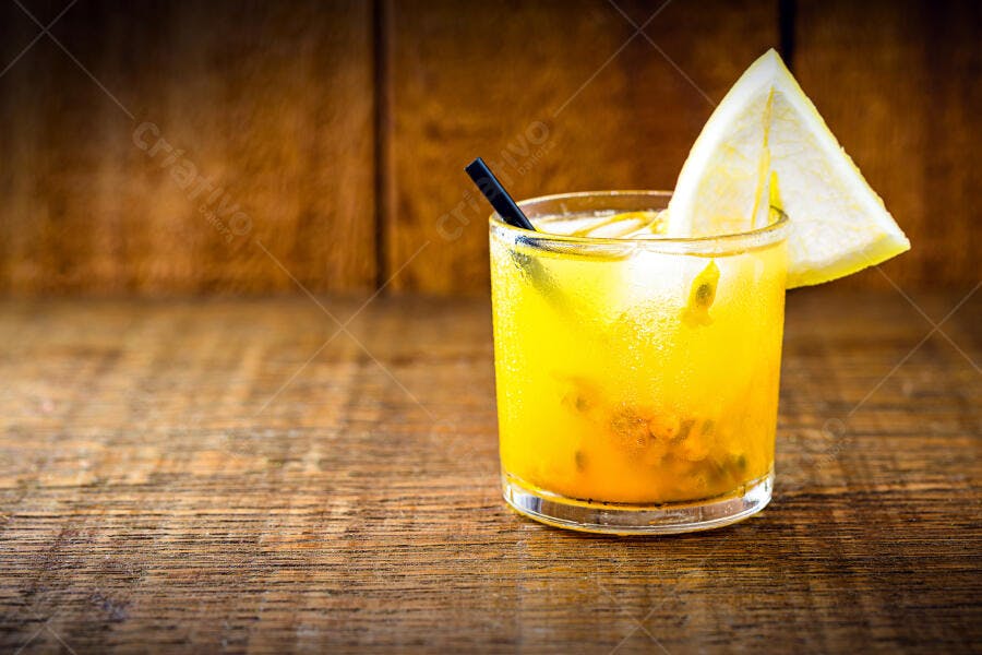 Caipirinha amarela de maracujá com gelo e fatia de limão em mesa de madeira