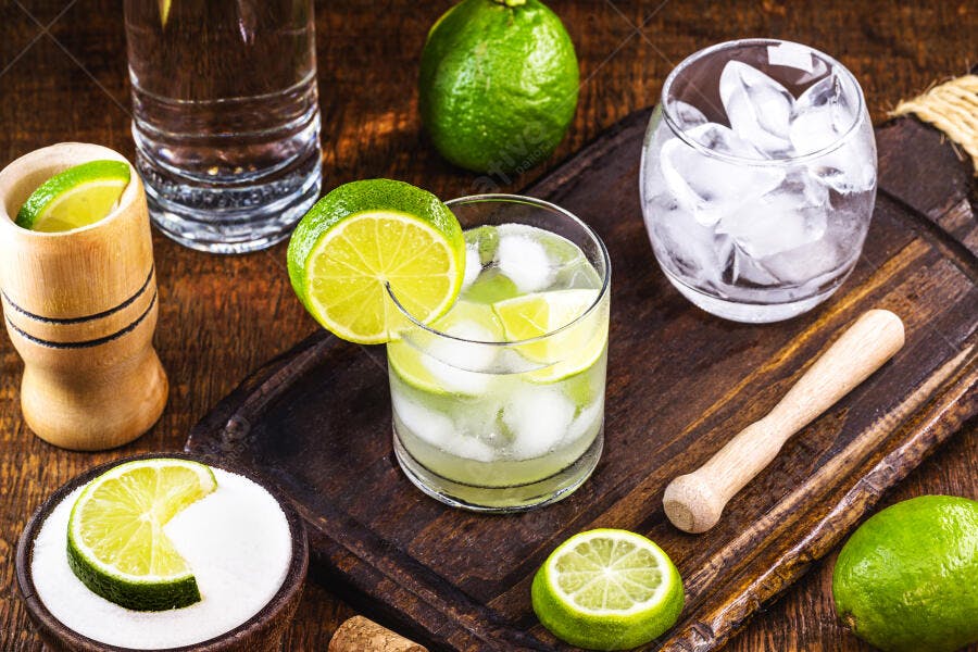 Caipirinha brasileira com limão e gelo em tábua de madeira rústica