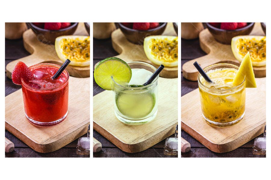 Três caipirinhas coloridas morango limão maracujá em tábuas de madeira rústica