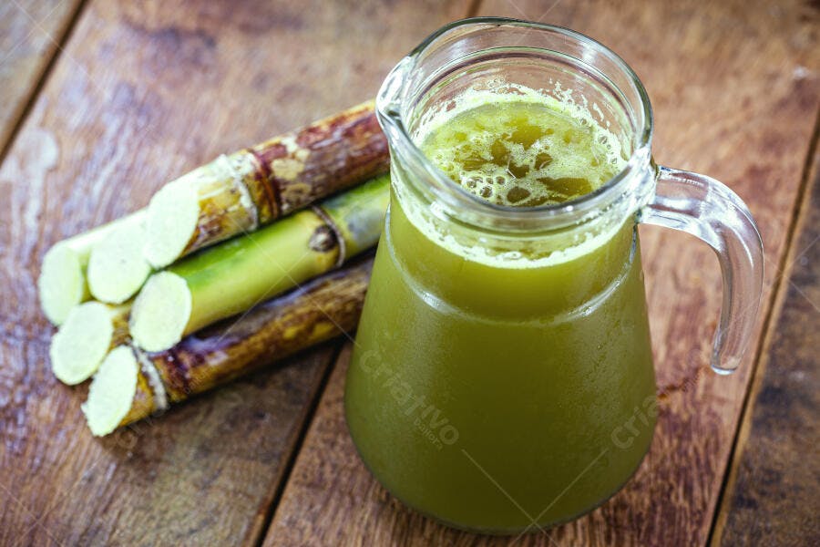 Jarra de caldo de cana verde fresco com talos de cana na mesa de madeira rústica