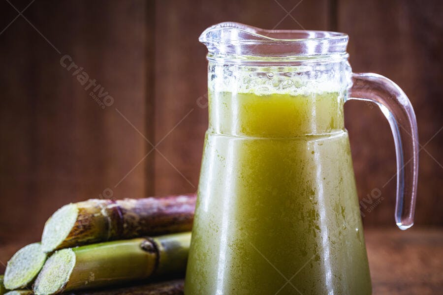 Jarra de caldo de cana verde gelado com pedaços de cana em fundo rústico de madeira