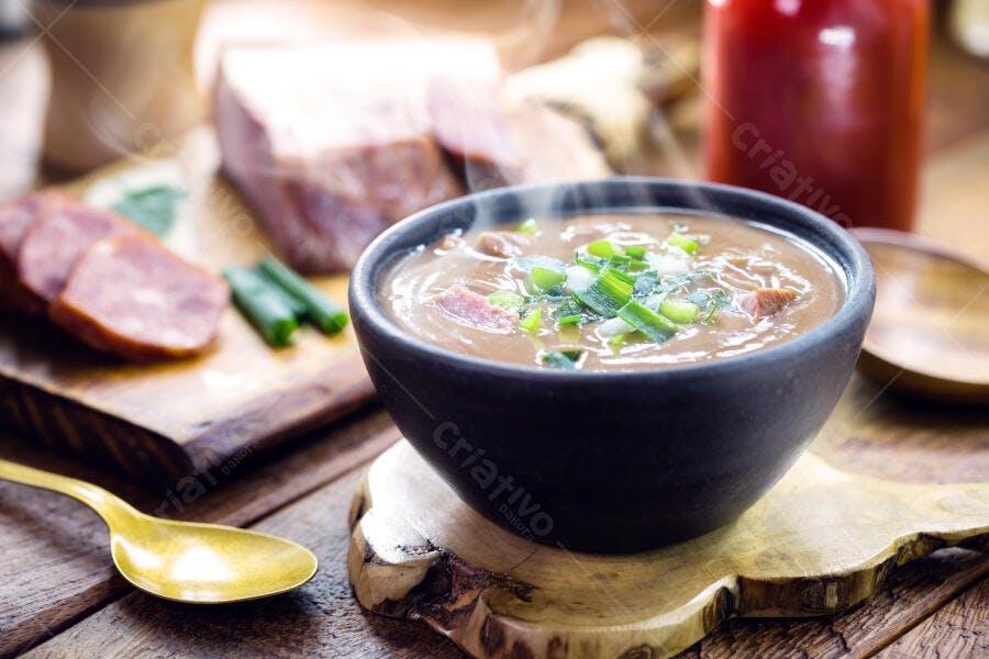 Cumbuca de sopa de feijão quente com linguiça e cebolinha em tábua rústica