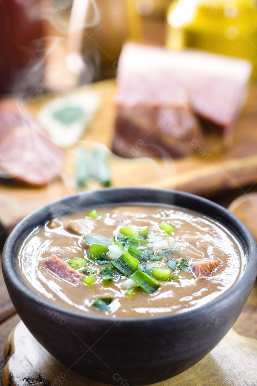 Caldo de feijão fumegante com carne e cebolinha verde em tigela rústica
