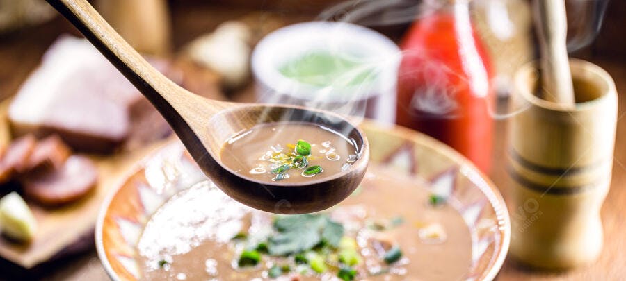 Caldo de feijão fumegante marrom com cheiro verde na colher de madeira