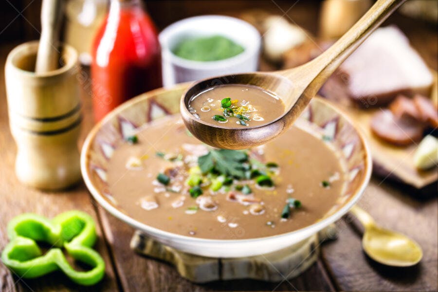 Caldo de feijão cremoso servido com colher de pau e cheiro verde