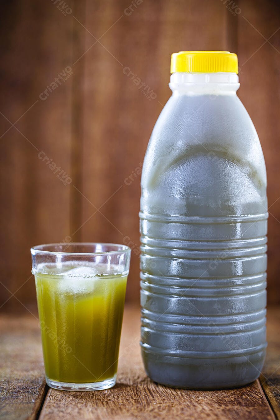 Garrafa e copo de suco verde fresco com gelo sobre madeira rústica