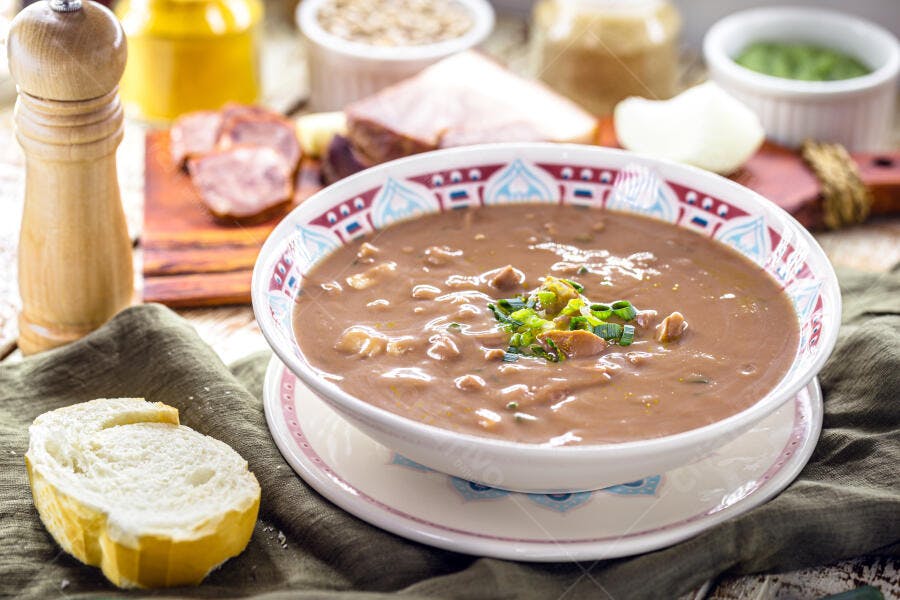 Tigela de caldo de feijão com linguiça e cebolinha em mesa rústica e pão fresco