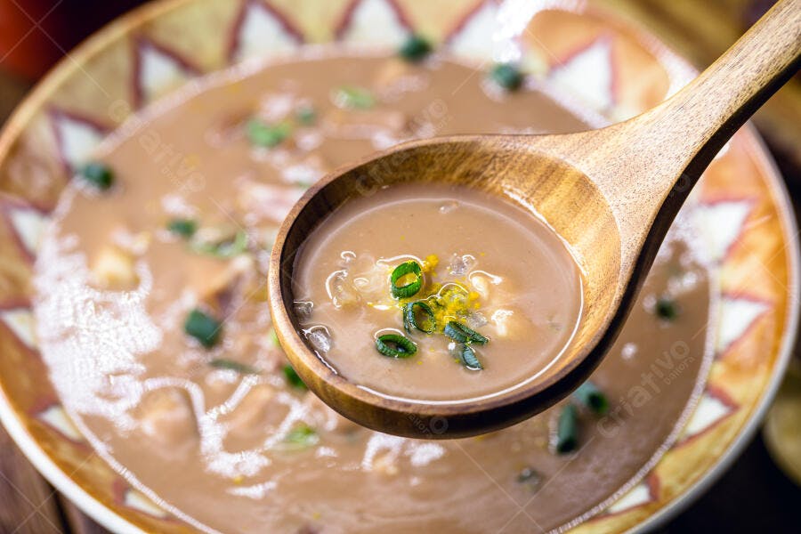 Sopa cremosa marrom claro com cheiro verde em colher de pau e tigela rústica