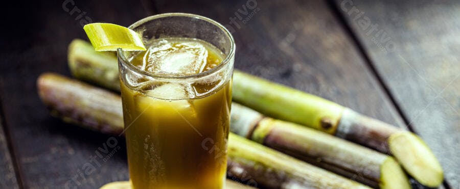 Caldo de cana fresco com gelo e cana de açúcar em mesa de madeira escura