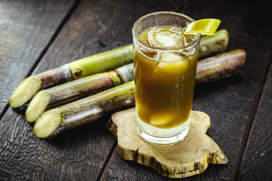 Caldo de cana refrescante com gelo e cana-de-açúcar fresca em mesa de madeira escura