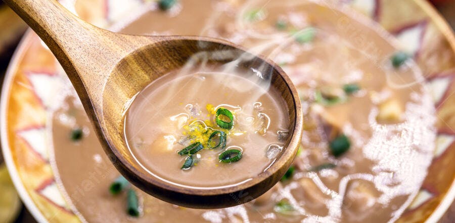Sopa cremosa marrom claro com cebolinha e vapor em concha de madeira quente