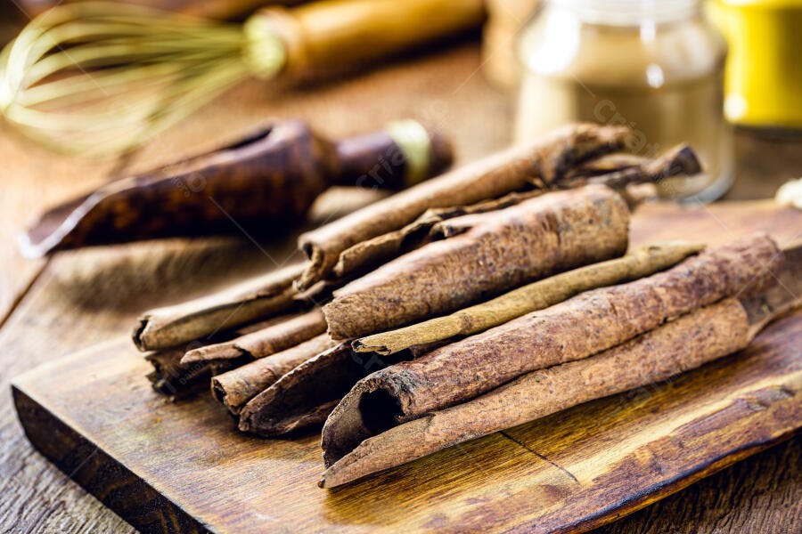 Canela em pau sobre tábua rústica de madeira com utensílios de cozinha e especiarias