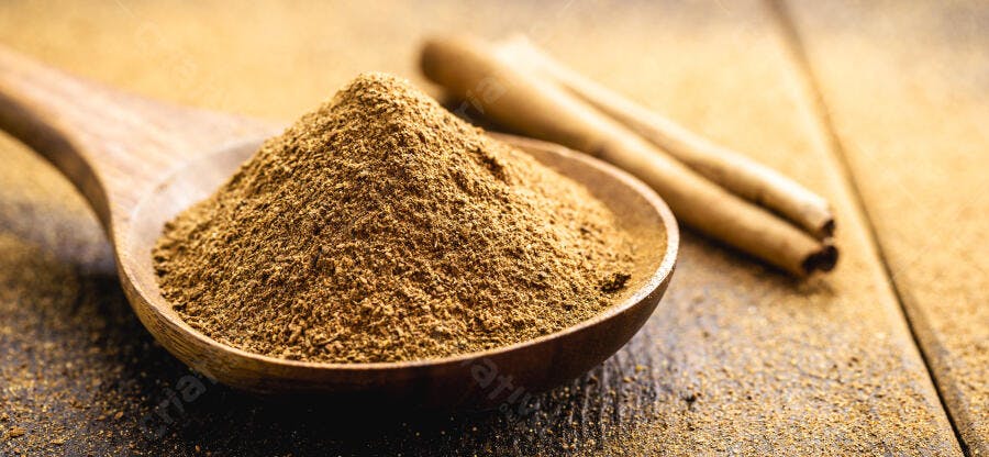 Canela em pó marrom dourado em colher de pau com paus no fundo rústico